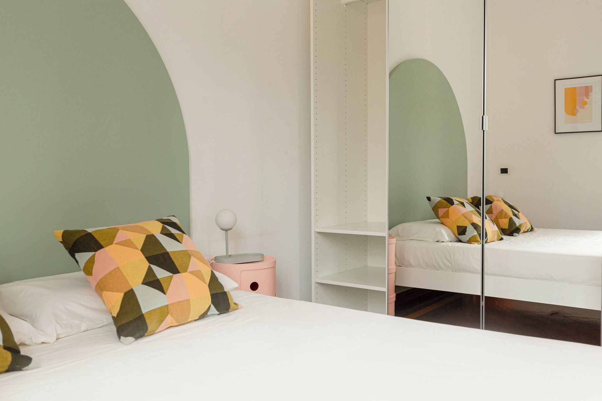 A bedroom with two beds, a pink nightstand, and a white wardrobe.