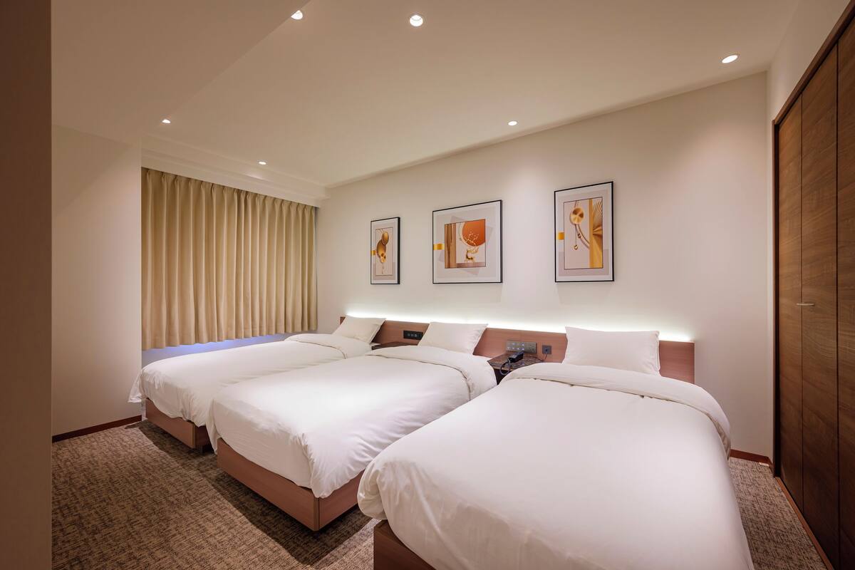 Une chambre d’hôtel avec deux lits, une grande fenêtre avec des rideaux et trois œuvres d’art encadrées accrochées au mur.