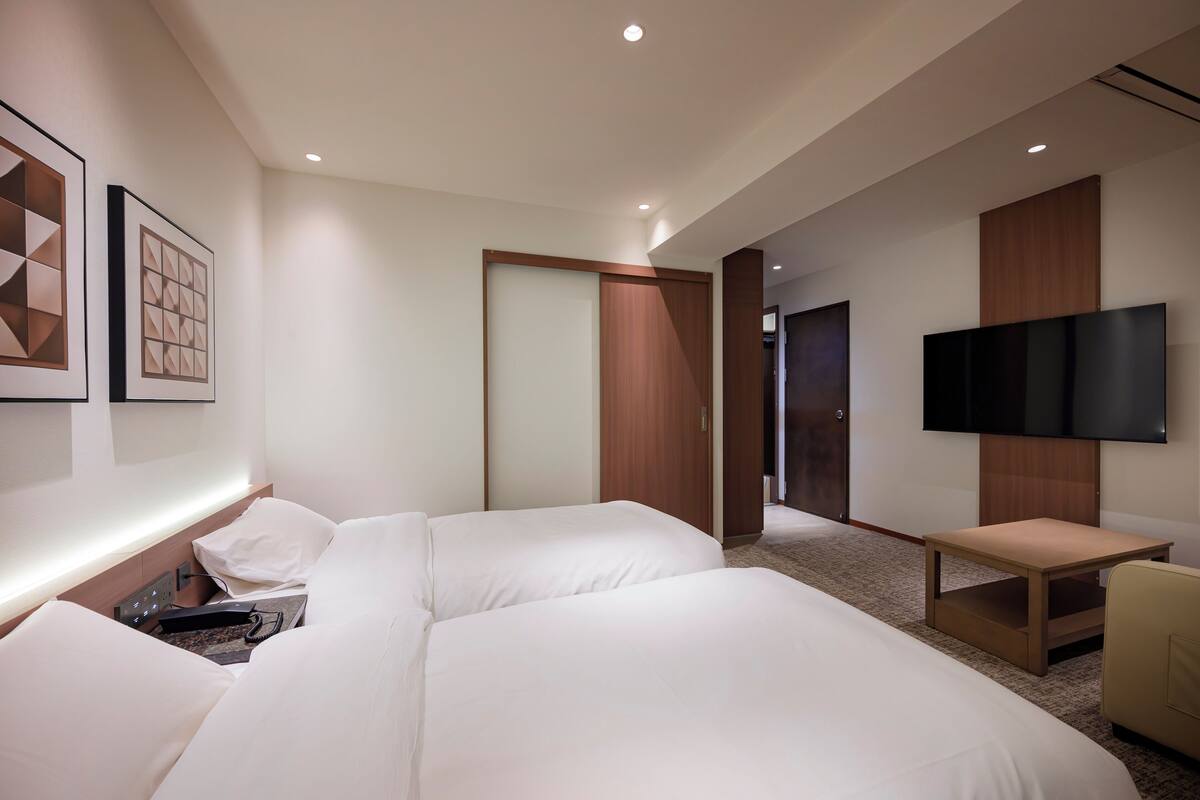 Une chambre d’hôtel moderne équipée de deux lits, d’un téléviseur à écran plat et d’une armoire en bois.