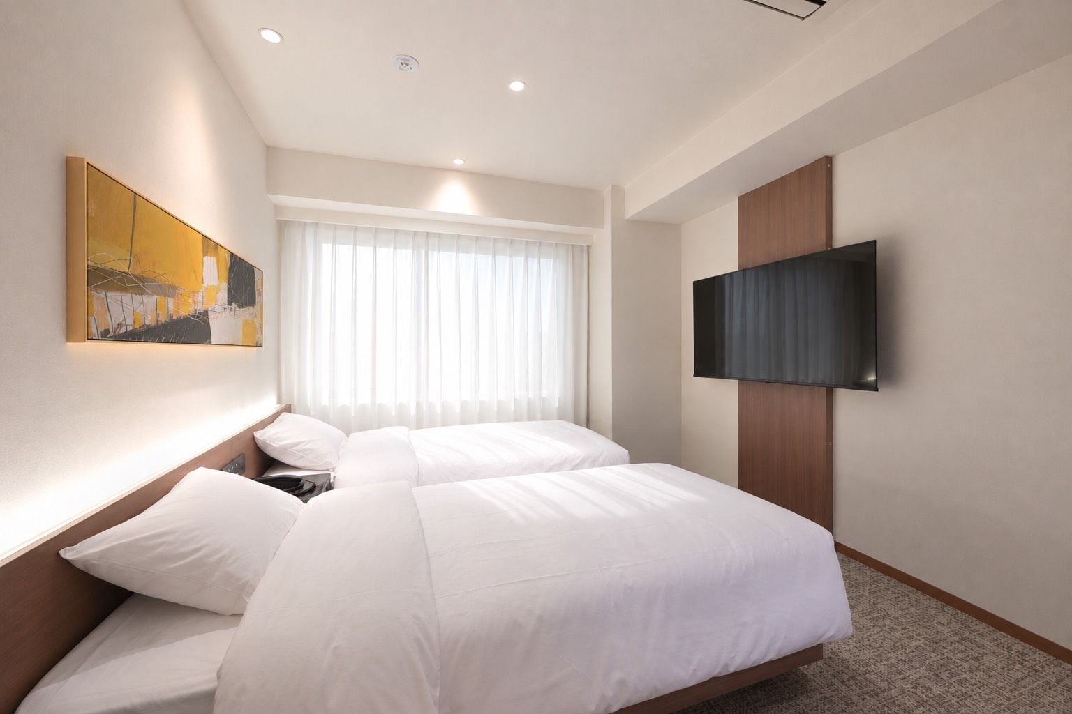 A hotel room with two beds, a flat-screen TV mounted on the wall, a painting on the wall, and a window with curtains.