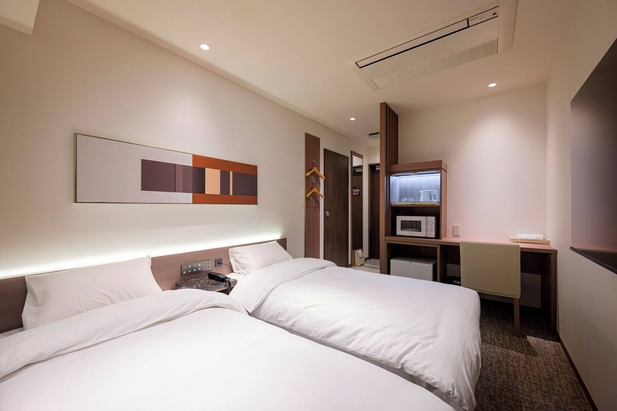 Une chambre d’hôtel avec deux lits, un bureau, un four à micro-ondes et une armoire.