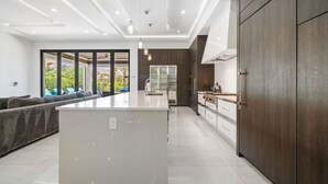 A modern kitchen with a central island, dark wood cabinets, and a large window offering a view of greenery.