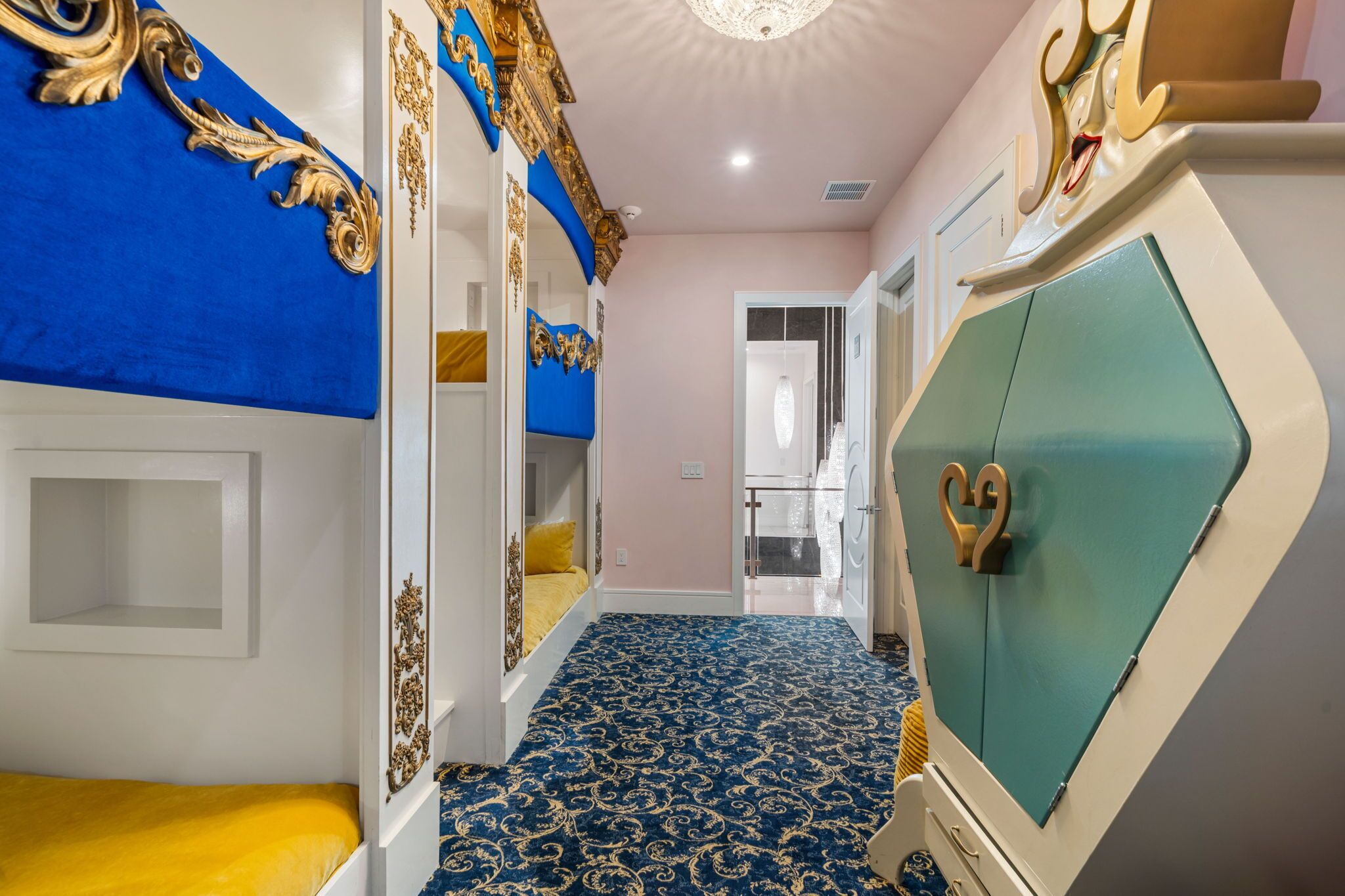 A narrow hallway with a blue patterned carpet, a bed with a yellow bedspread, and a wardrobe with a teal door.