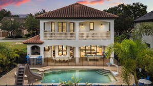 Una casa de dos pisos con piscina, mobiliario exterior y un tobogán.
