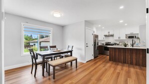 Une cuisine moderne avec des meubles blancs, un îlot central en bois et un coin repas doté d’une banquette.