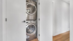 Une buanderie moderne et compacte, dotée de deux machines à laver à chargement frontal en acier inoxydable, de murs blancs et d’un plancher en bois.