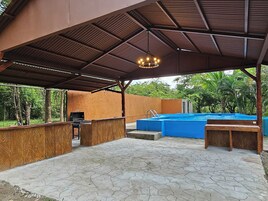 Un área de piscina al aire libre con un porche cubierto, una parrilla y una terraza de madera.