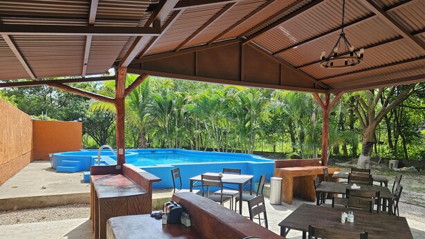 Área de piscina ao ar livre com bar e assentos sob um pavilhão coberto.