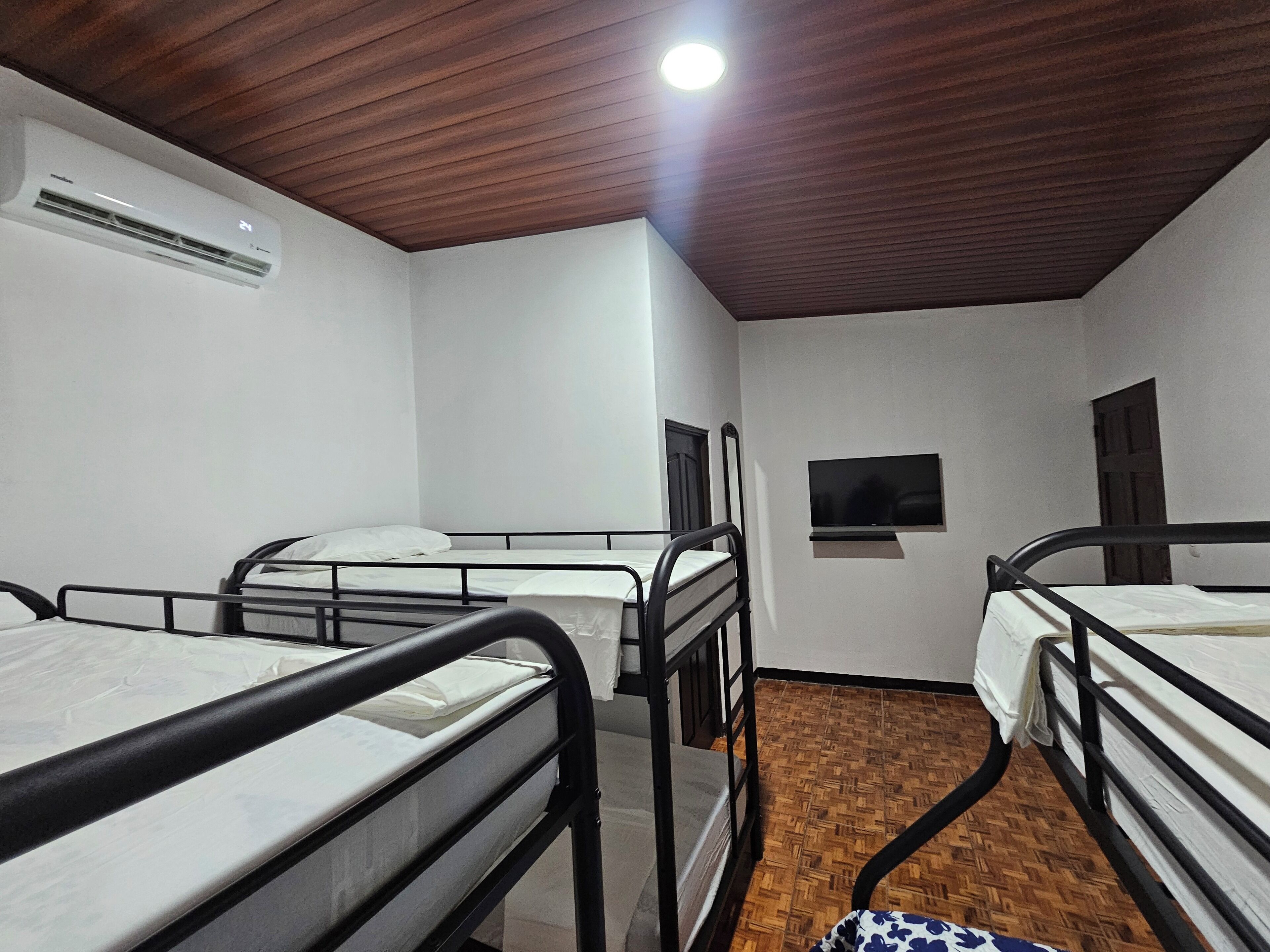 Un dormitorio con tres literas, techo de madera, aire acondicionado de pared y televisor en la pared.
