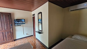 Quarto de hotel com teto de madeira, televisão presa na parede, cama com roupa de cama branca e porta de madeira.