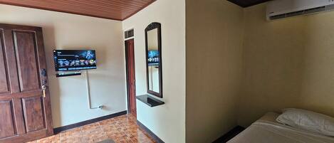 Habitación de hotel con techo de madera, televisor montado en la pared, cama con ropa de cama blanca y puerta de madera.
