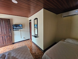 A hotel room with a wooden ceiling, a television mounted on the wall, a bed with white bedding, and a wooden door.