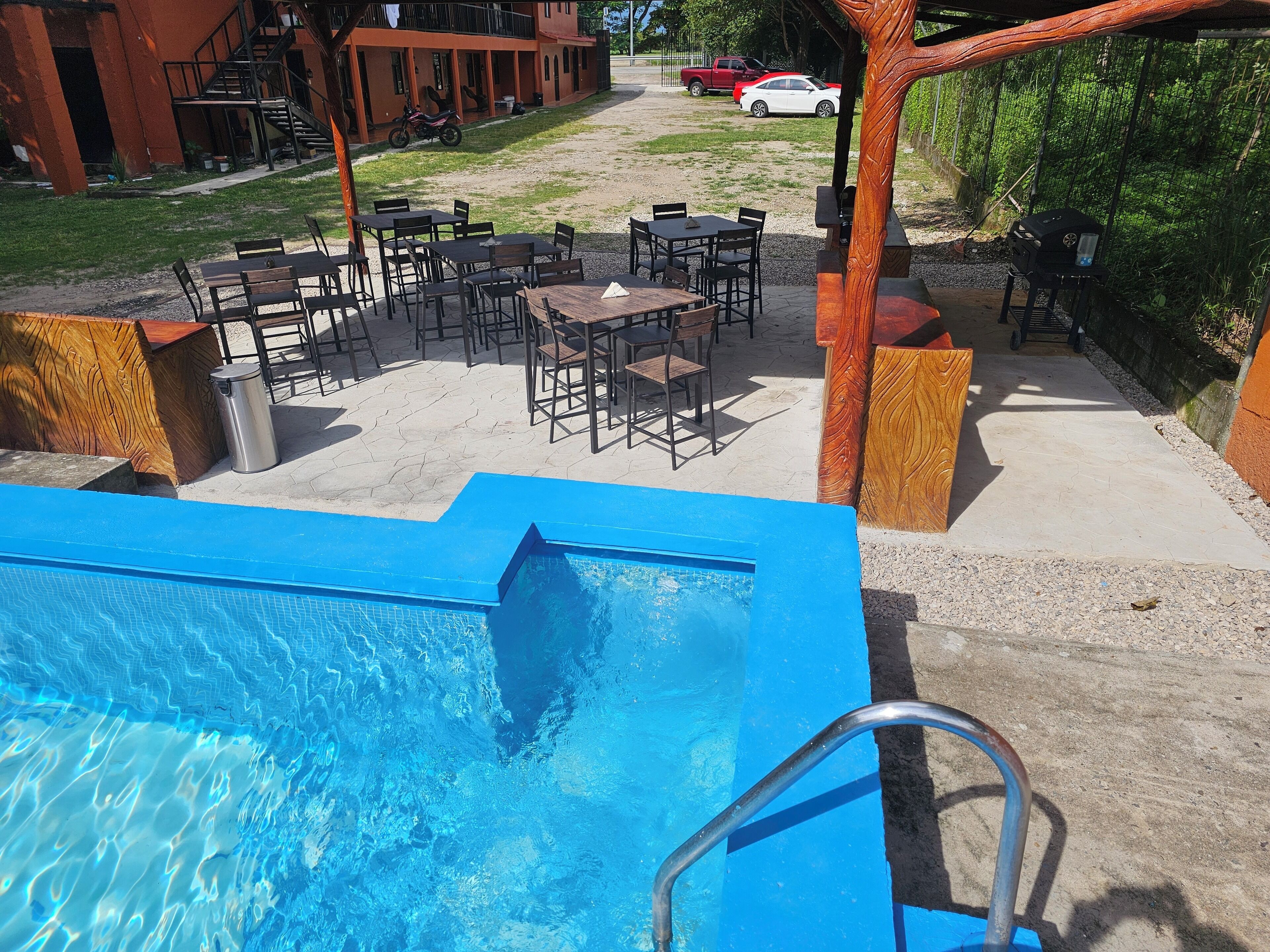 Uma área de piscina com piscina azul, mobiliário de exterior e um edifício ao fundo.