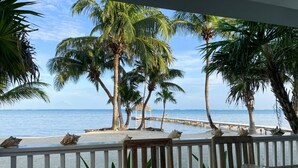 A wooden table with two glass bowls containing shells, overlooking a beach with palm trees and a pier. - Casa Maravilla,Sleeps 8@SapphireBeachResort (Not available)