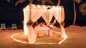 A beachside tent with a table set for two, surrounded by palm trees and string lights. - Casa Maravilla,Sleeps 8@SapphireBeachResort (Not available)