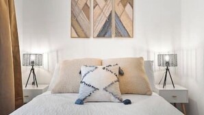 A neatly made bed with a white duvet, two pillows, and a decorative throw. There are two bedside tables with lamps on either side of the bed. - DesertDreamscape Sauna Cold Plunge SPA 3 min to JT (Twentynine Palms)