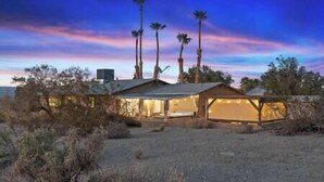 A modern, single-story house with a flat roof, surrounded by desert vegetation and palm trees. - DesertDreamscape Sauna Cold Plunge SPA 3 min to JT (Twentynine Palms)