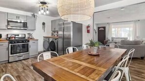 A modern kitchen with stainless steel appliances, a wooden dining table, and a large pendant light. - DesertDreamscape Sauna Cold Plunge SPA 3 min to JT (Twentynine Palms)