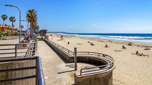 Una playa con un paseo marítimo de concreto, palmeras y una torre de salvavidas.
