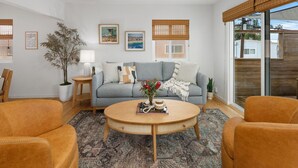 Una sala de estar con un sofá gris, dos sillones, una mesa de centro y un amplio ventanal con persianas.