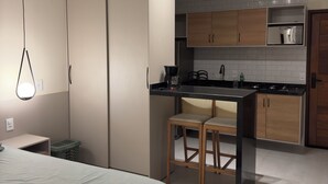 A modern bedroom with a bed, a nightstand, and a desk. Adjacent to the bedroom is a kitchenette with wooden cabinets, a countertop, and a sink. - FLAT IN ALTER DO CHÃO (Alter do Chão)