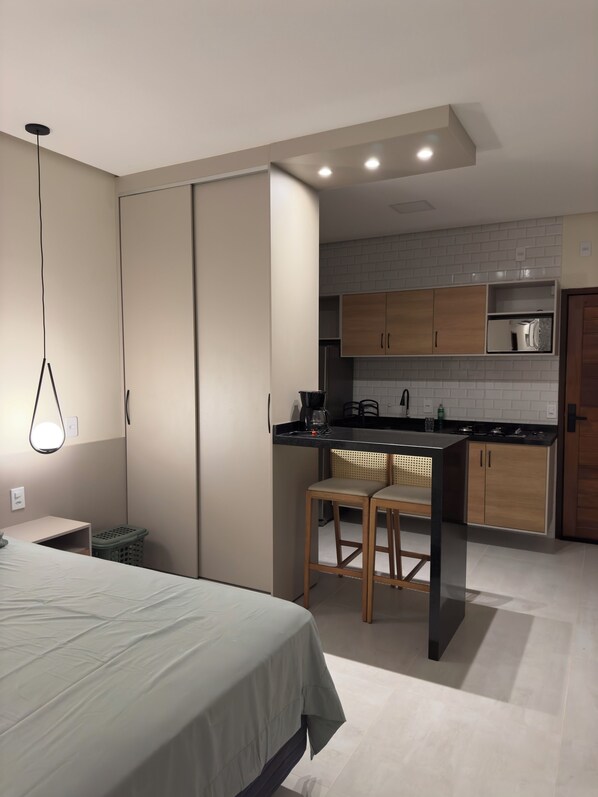 Een moderne slaapkamer met een bed, nachtkastje en bureau. Grenzend aan de slaapkamer bevindt zich een kitchenette met houten kastjes, een aanrecht en een spoelbak.