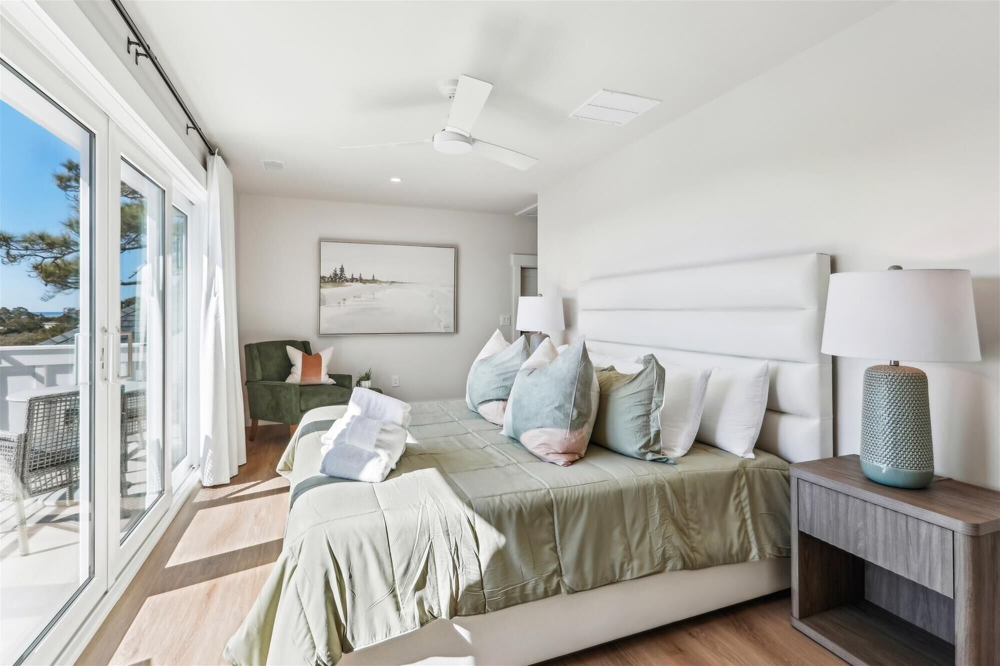Une chambre moderne avec un grand lit, une vue à travers la porte vitrée et un ventilateur de plafond.