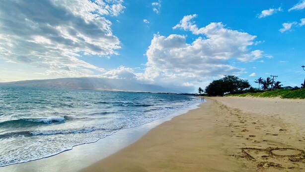 A beach with a sandy shore, ocean waves, and a clear sky with clouds.