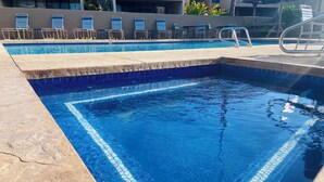 A swimming pool with blue mosaic tiles, lounge chairs, and a poolside area.
