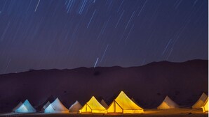 File di tende illuminate nel deserto di notte, con scie di stelle nel cielo.