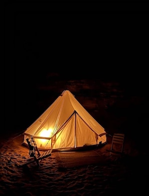 A tent set up in a sandy area at night with a light source inside. - Safari Algeria Camp (Djanet)