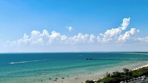 Une plage avec une eau d’un bleu limpide, une jetée et une route où circulent des voitures.