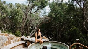 Un espace de sources chaudes doté d’une terrasse en bois et de murs en pierre, entouré d’arbres.