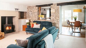 Un salon chaleureux avec un mur en pierre, une cheminée, un canapé bleu et un coin repas comprenant des chaises et une table.