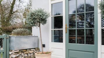 A white building with a green door and windows, a stone wall, and a potted tree.