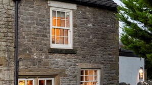 A stone building with two windows, one with a visible interior light.