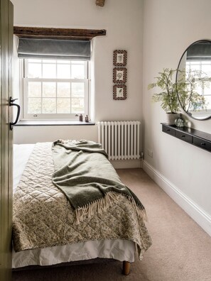 Um quarto com uma cama, janela, radiador, espelho e uma planta.