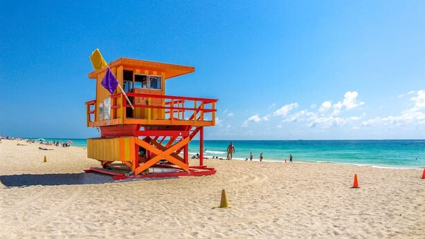 Una torre de salvavidas en una playa con cielos despejados y aguas tranquilas.