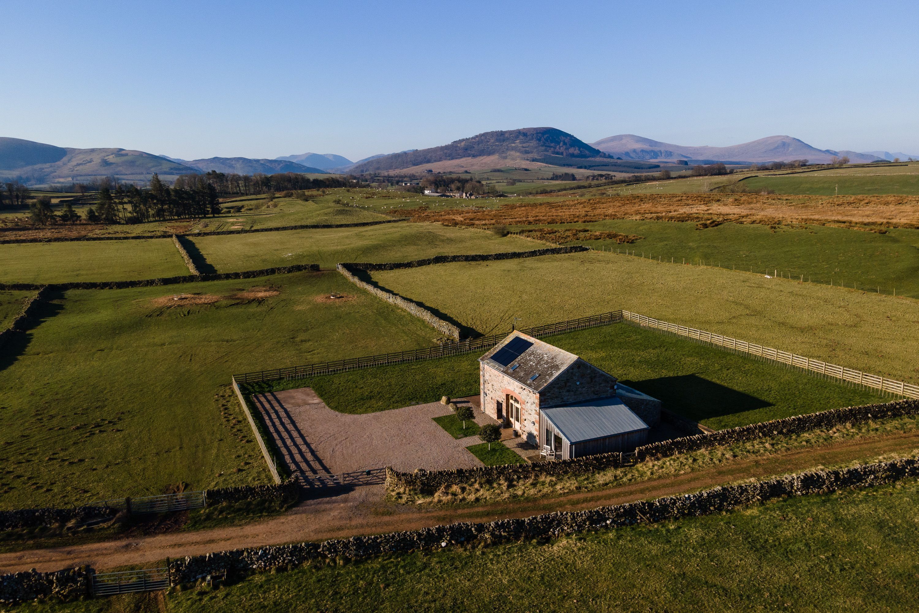 A rural landscape with a stone house surrounded by fields and stone walls.