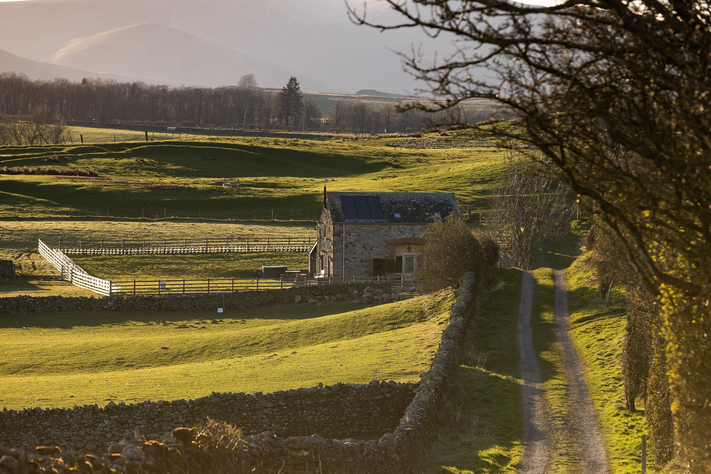 Ländliche Landschaft mit einem Steinhaus, einem eingezäunten Feld und einer Steinmauer.