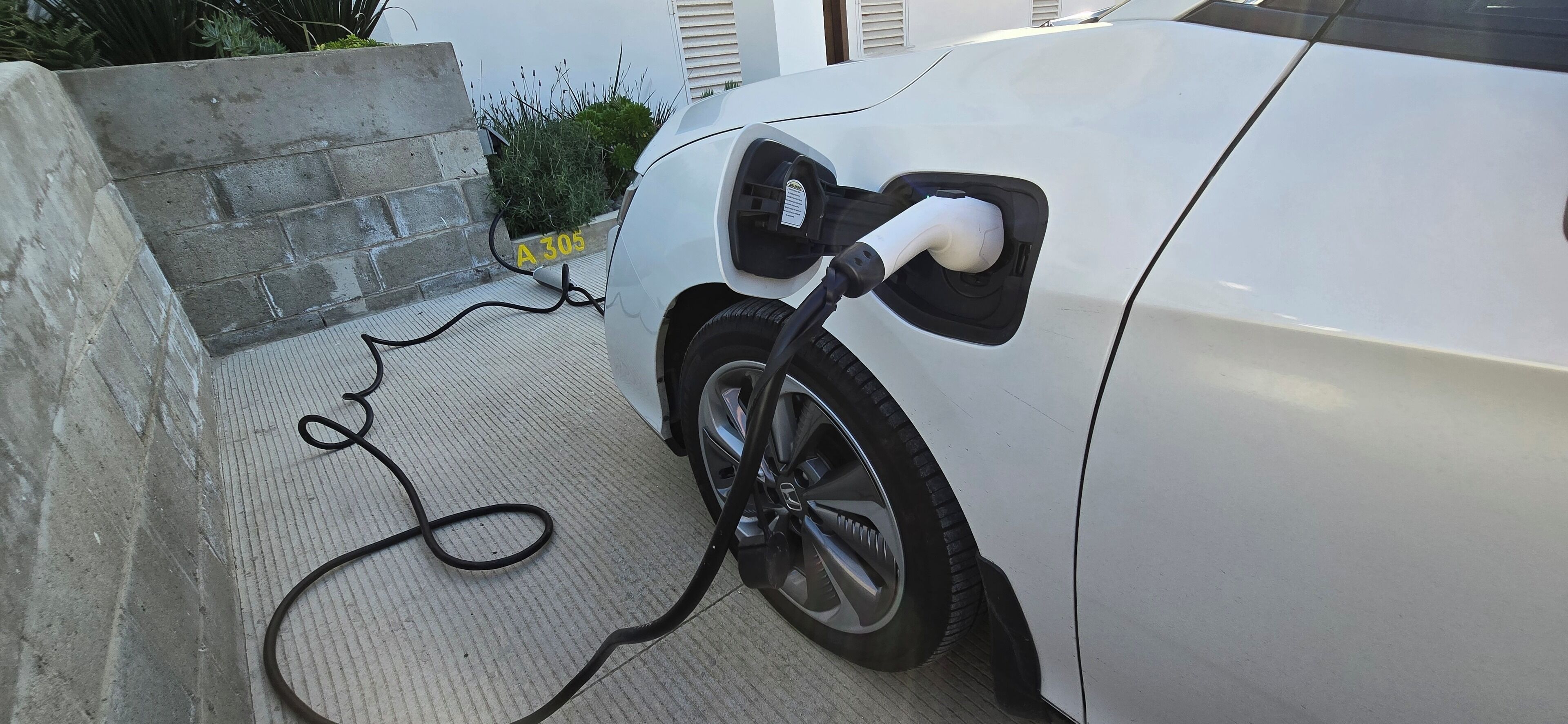 Ein weißes Auto ist an einer Ladestation geparkt und über ein Kabel mit Strom verbunden.