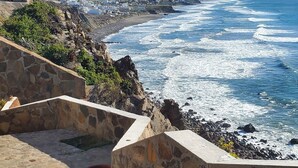 Un sentier de pierres qui longe la côte et mène à une plage rocheuse, offrant une vue sur l’océan et les collines lointaines.