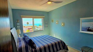 Une chambre avec un lit, une fenêtre donnant sur la mer et un ventilateur de plafond.