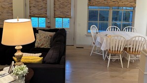 A living room with a black sofa, a table with a lamp, and a dining area with white chairs and a table.