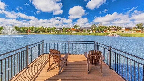 A wooden deck with two Adirondack chairs overlooking a lake with houses in the background.
