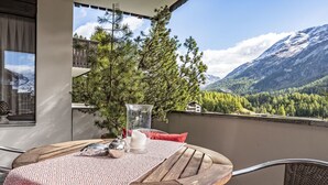A balcony with a wooden table, a glass vase, and a red cushion. A pine tree and a mountain view are visible in the background. - Chesa Trais Dschembers by Interhome (Champfer)