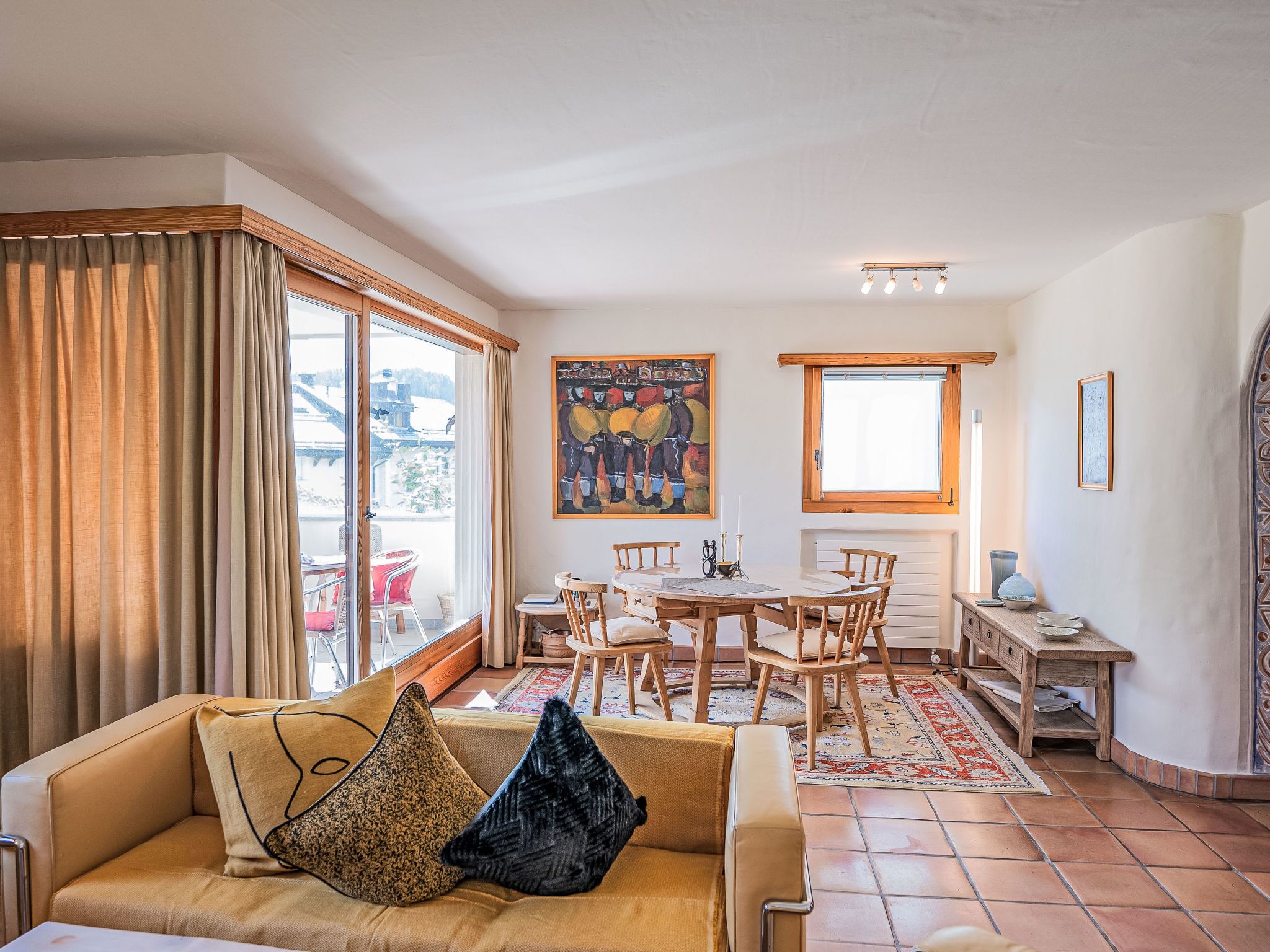 A cozy living room with a sofa, a dining table with chairs, a painting on the wall, and a window with curtains.