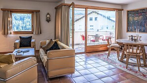 A living room with a sofa, chairs, a dining table, and a view of a building through a glass door. - Chesa Trais Dschembers by Interhome (Champfer)