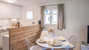 A modern kitchen with white cabinets, a wooden accent wall, and a dining area with a round table set for two.