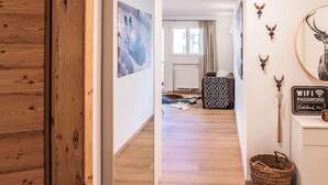 A hallway with wooden flooring, a white wall with a framed picture, a brown leather chair, a black and white patterned blanket, a cowhide rug, and a wicker basket.